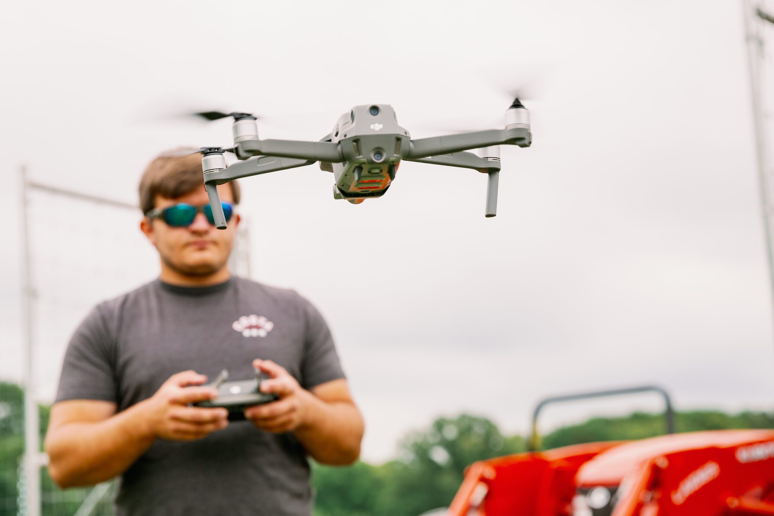 A quadricopter drone/uav being piloted by a student wearing a grey t-shirt and sunglasses